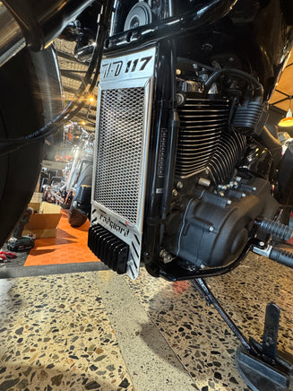 Close-up of a motorcycle engine with visible branding on a speckled floor with a rad guard in polished fitted