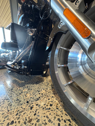 Close-up of a motorcycle wheel and suspension on a textured surface with a black rad guard fitted to a Harley Davidson Heritage Classic 117. 