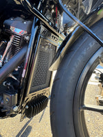 Close-up of a motorcycle's engine and exhaust system with a tire in the background also showing the radguard fitted for a perfect fit in black 