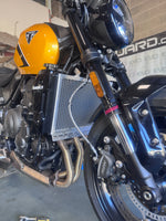 Close-up of a motorcycle's engine and handlebar with a helmet on the handlebar with a rad guard radiator guard fitted like a glove for a Triumph Trident 660 