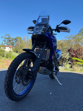 Blue motorcycle on a road with trees and clear sky in the background showing a polished alloy Rad Guard fitted offering protection from rocks and road debris
