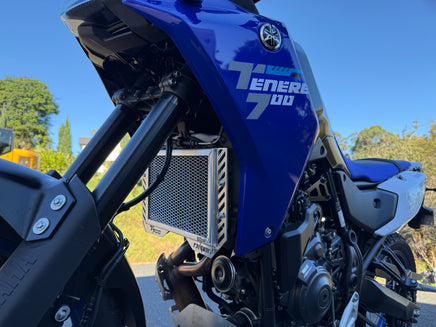 Close-up of a blue motorcycle with visible branding against a blurred natural background. Showing a Rad Guard Radiator guard fitted and giving protection to the radiator core. Tough and built to last